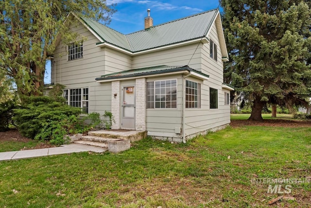 traditional-style house featuring metal roof, a front lawn, and a chimney