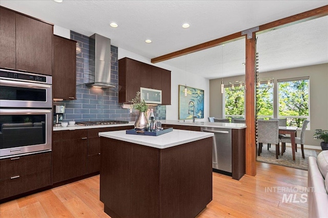 3602 N Prospect Way, Garden City, ID 83714 - kitchen featuring wall chimney range hood, appliances with stainless steel finishes, light countertops, a center island, and dark brown cabinetry