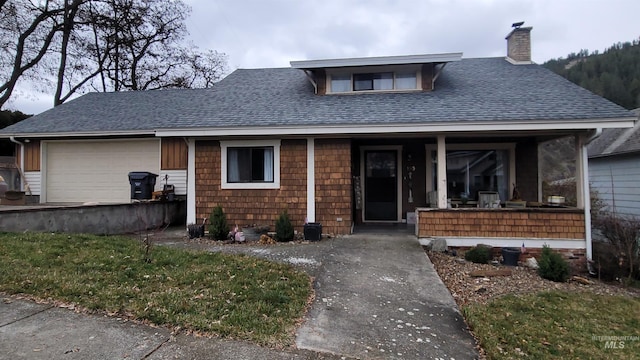 view of front facade featuring a garage, a chimney, covered porch, and a shingled roof