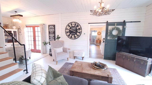 living area featuring a notable chandelier, a barn door, french doors, wood walls, and stairs