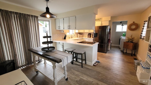 kitchen featuring light wood-type flooring, a sink, a peninsula, decorative backsplash, and black refrigerator with ice dispenser