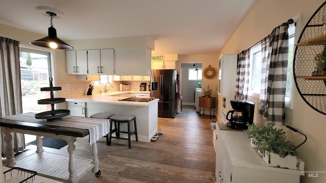 kitchen with wood finished floors, a peninsula, decorative backsplash, light countertops, and black refrigerator with ice dispenser