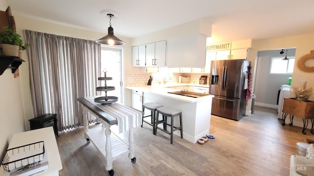 kitchen featuring light wood finished floors, tasteful backsplash, stainless steel fridge, a peninsula, and light countertops