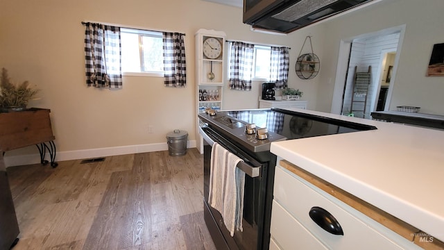 kitchen with light wood finished floors, visible vents, baseboards, electric stove, and white cabinets