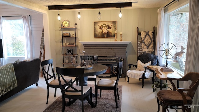 dining area with wooden walls, beamed ceiling, a fireplace, wood finished floors, and a textured ceiling