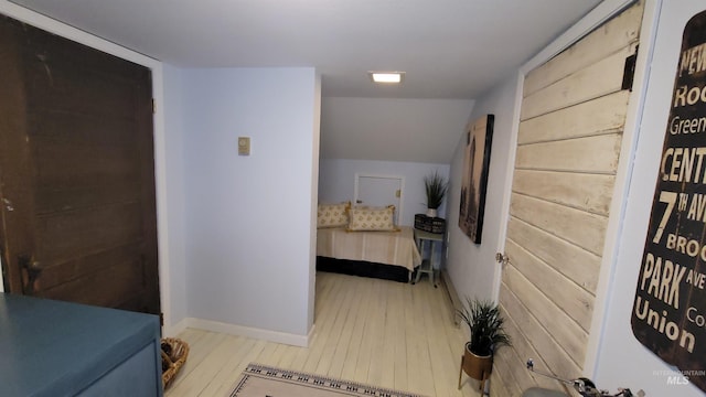 hallway featuring baseboards, vaulted ceiling, and light wood finished floors