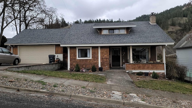 view of front facade with a chimney, a porch, a shingled roof, and an attached garage