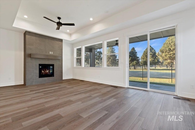 unfurnished living room with a fireplace, hardwood / wood-style flooring, a raised ceiling, and ceiling fan