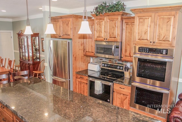 kitchen featuring pendant lighting, backsplash, stainless steel appliances, and dark stone countertops