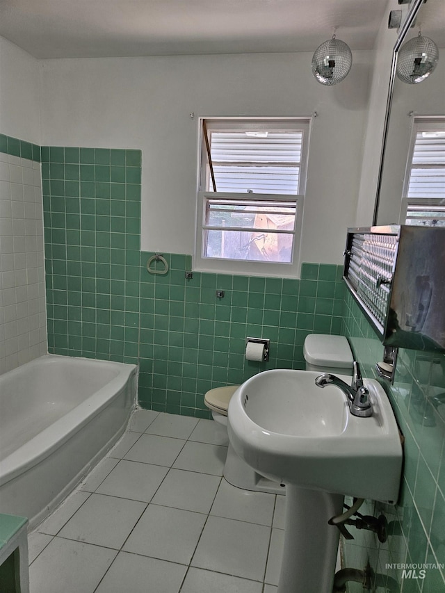 207 N Main St, Homedale, ID 83628 - bathroom featuring tile walls, tile patterned floors, toilet, a bath, and wainscoting