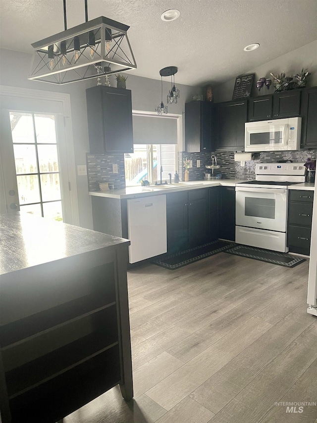 kitchen featuring tasteful backsplash, a textured ceiling, white appliances, light hardwood / wood-style floors, and hanging light fixtures