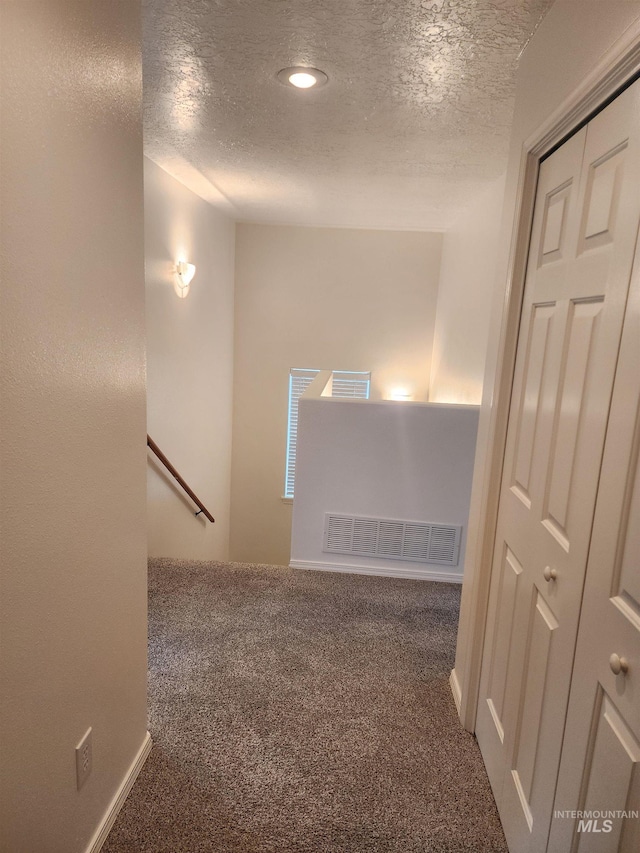 corridor with a textured ceiling and dark carpet