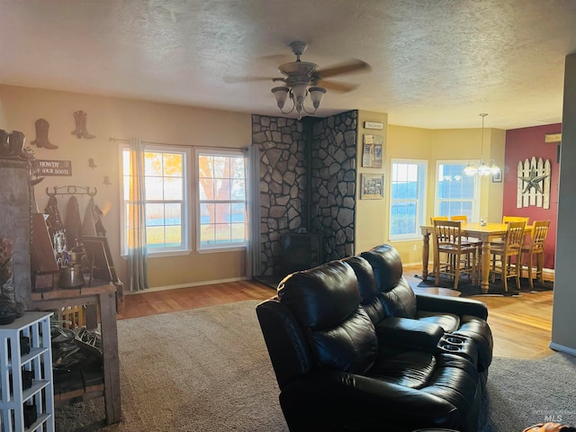 living room with ceiling fan with notable chandelier, a wood stove, a textured ceiling, and hardwood / wood-style floors