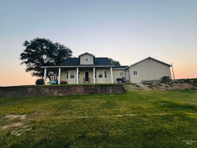 back house at dusk with a porch and a yard