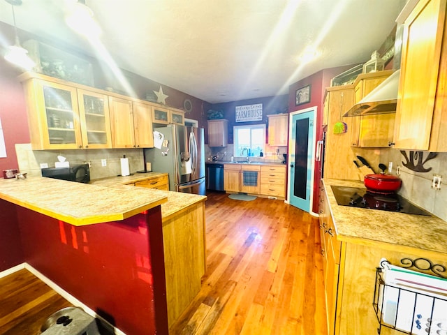 kitchen with light wood-type flooring, kitchen peninsula, wall chimney range hood, decorative backsplash, and appliances with stainless steel finishes