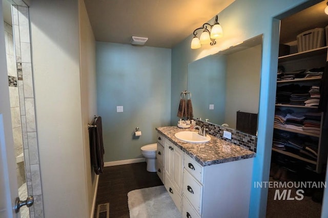 bathroom featuring toilet, baseboards, visible vents, vanity, and a walk in closet