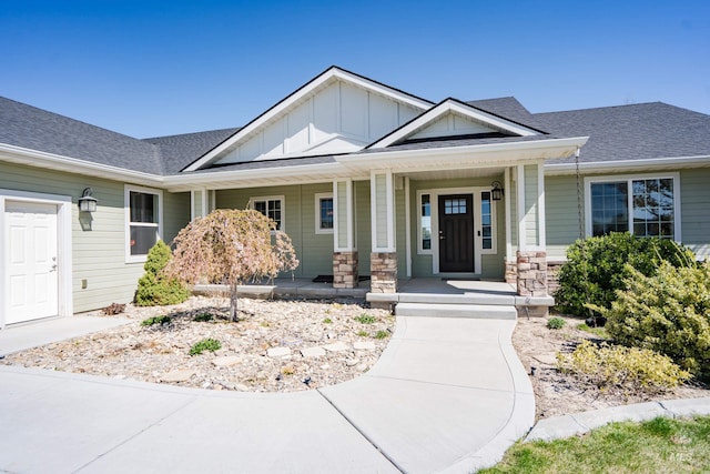 craftsman inspired home featuring board and batten siding, covered porch, stone siding, and roof with shingles
