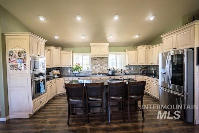 kitchen with a kitchen island with sink, appliances with stainless steel finishes, tasteful backsplash, and a breakfast bar