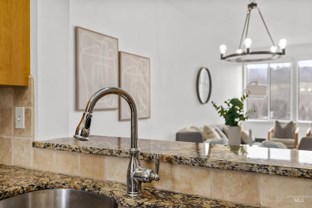 details featuring decorative backsplash, dark stone counters, a sink, and a chandelier