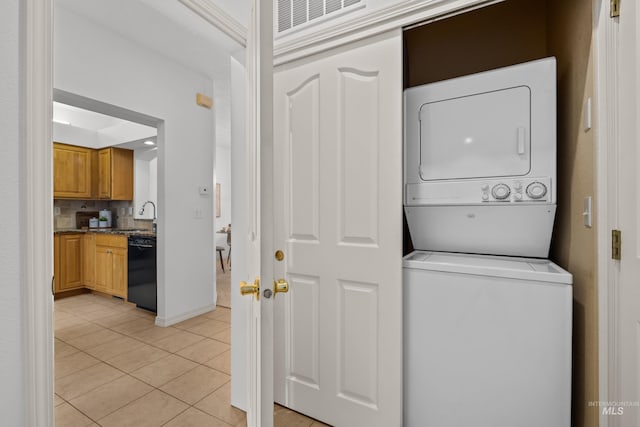 laundry room with light tile patterned floors, a sink, stacked washing maching and dryer, laundry area, and baseboards