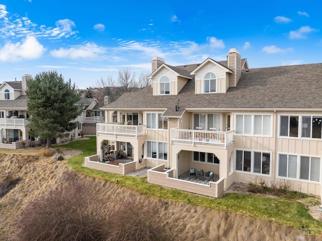 rear view of property featuring a shingled roof, board and batten siding, a chimney, and a balcony