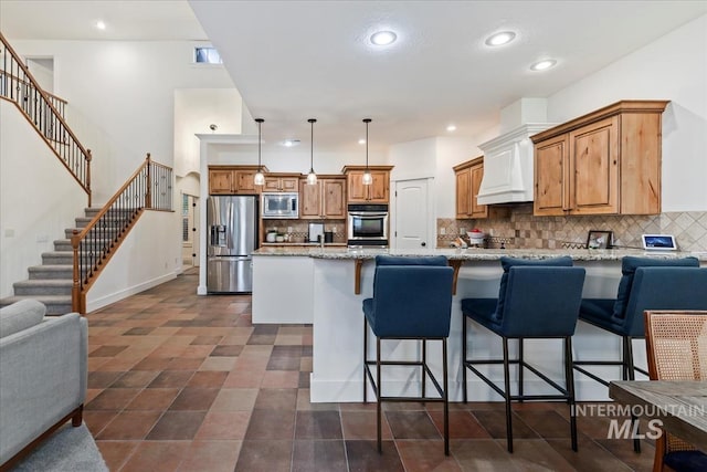 kitchen featuring light stone counters, a breakfast bar, custom range hood, appliances with stainless steel finishes, and tasteful backsplash