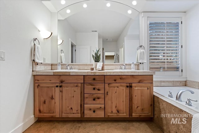 full bathroom featuring double vanity, a bathtub, baseboards, and a sink