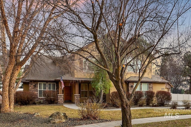 view of front of home featuring a front yard, a porch, fence, and stone siding