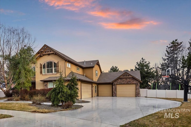 view of front of property with stone siding, stucco siding, driveway, and fence