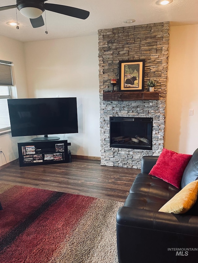 living room featuring ceiling fan, wood-type flooring, and a stone fireplace