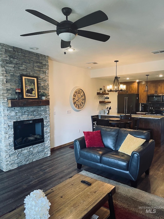 living room featuring dark wood-type flooring, a fireplace, and ceiling fan with notable chandelier