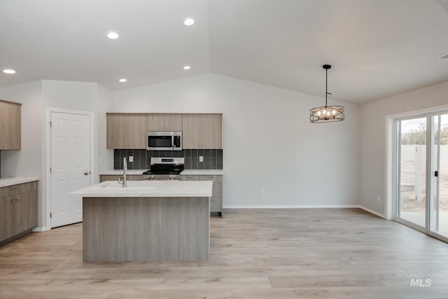 kitchen with appliances with stainless steel finishes, decorative backsplash, sink, an island with sink, and vaulted ceiling