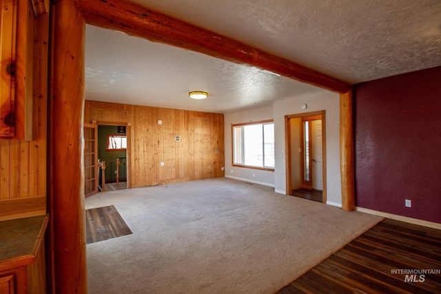 unfurnished living room featuring dark carpet, beam ceiling, wooden walls, and a textured ceiling