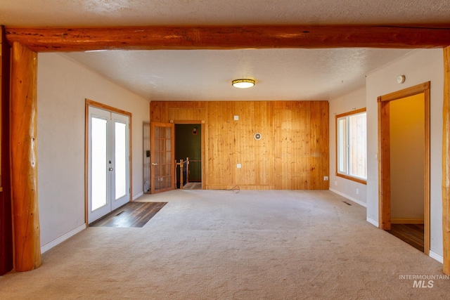 spare room featuring wooden walls, beam ceiling, light carpet, and a textured ceiling