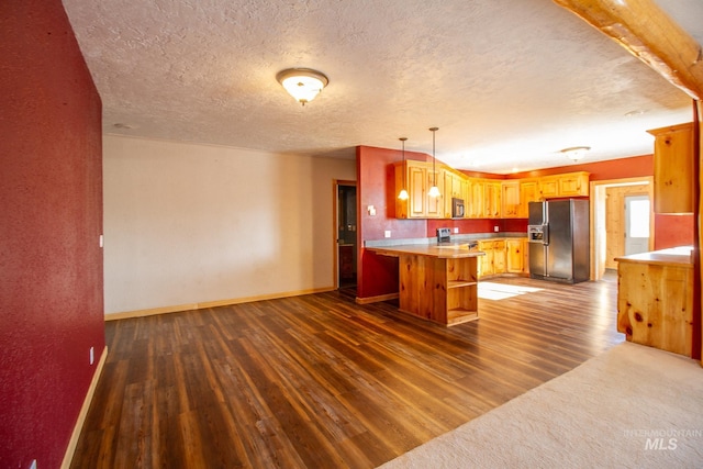 kitchen with appliances with stainless steel finishes, hanging light fixtures, kitchen peninsula, dark wood-type flooring, and a textured ceiling