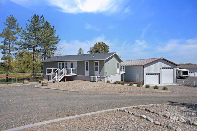 ranch-style home with a detached garage, central air condition unit, dirt driveway, fence, and metal roof