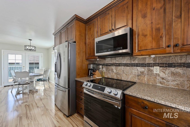 kitchen featuring tasteful backsplash, light wood-type flooring, appliances with stainless steel finishes, a notable chandelier, and light stone countertops