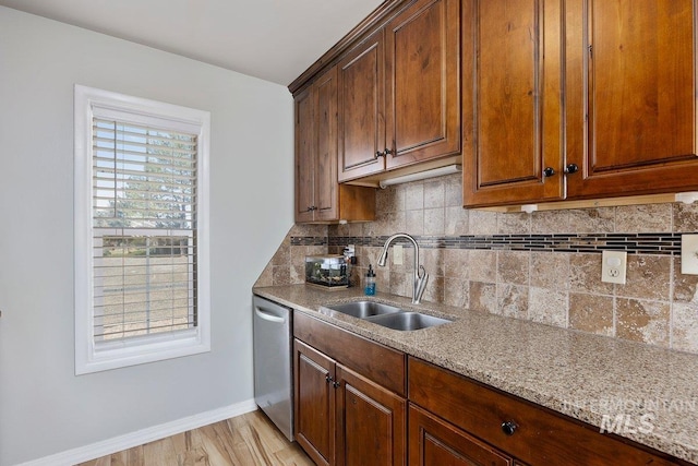 kitchen featuring backsplash, stainless steel dishwasher, a sink, light stone countertops, and baseboards