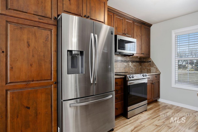 kitchen featuring stainless steel appliances, light wood-type flooring, stone counters, baseboards, and tasteful backsplash