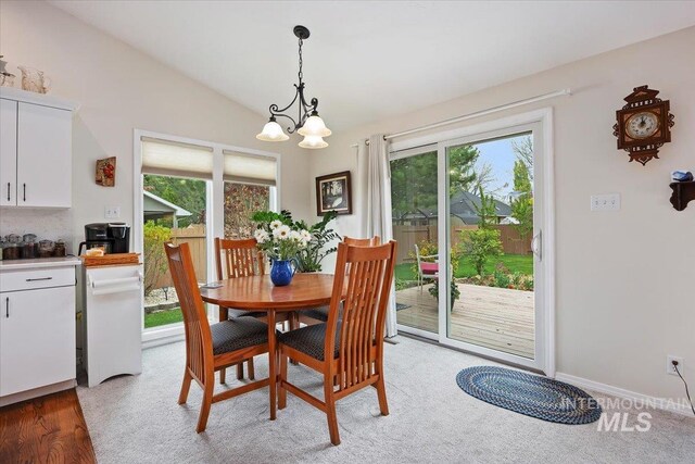 dining area featuring healthy amount of natural light, vaulted ceiling, a chandelier, and light carpet