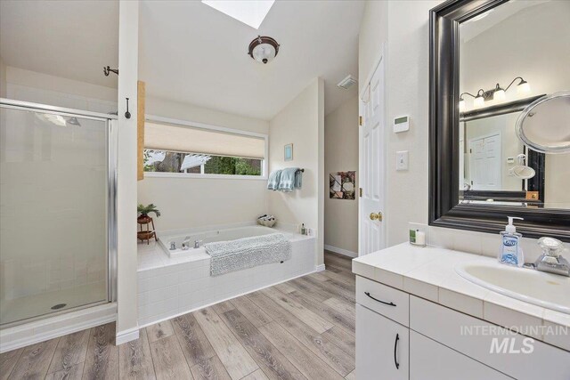 full bathroom with a skylight, a stall shower, a bath, wood finished floors, and vanity