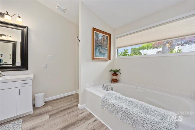 full bath with vanity, a garden tub, wood finished floors, and vaulted ceiling