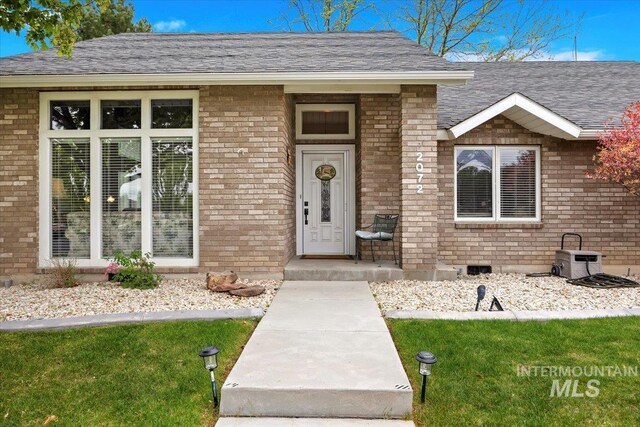 property entrance featuring brick siding, a shingled roof, and a lawn