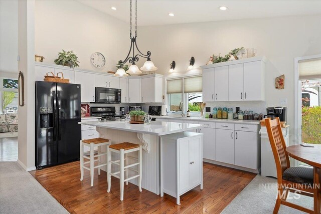kitchen with black appliances, high vaulted ceiling, a kitchen island, white cabinetry, and light countertops