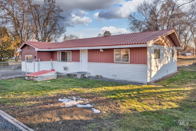 view of front of home featuring a tiled roof, a chimney, a front yard, and fence