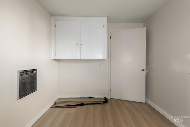 clothes washing area with heating unit, wood finished floors, and baseboards