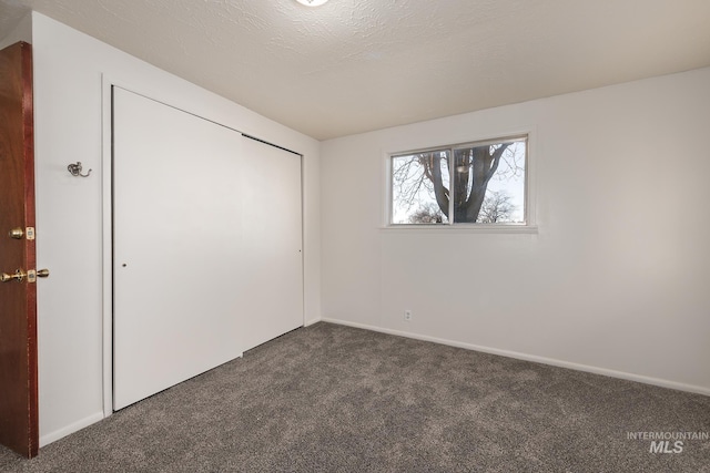 unfurnished bedroom with a closet, dark carpet, and a textured ceiling