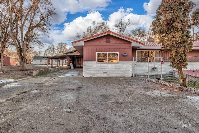 view of front of property featuring an attached carport, board and batten siding, fence, stone siding, and driveway