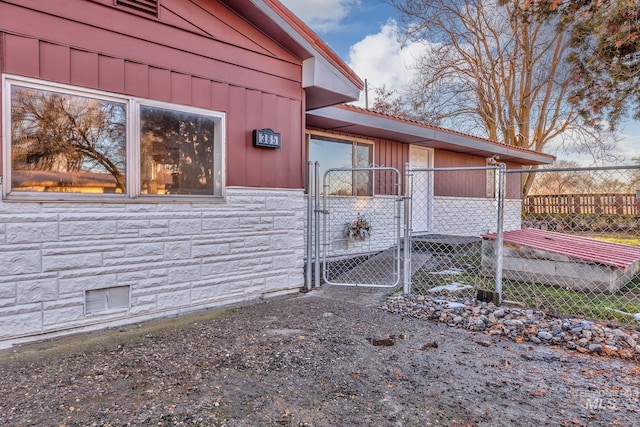 view of property exterior featuring stone siding, fence, and a gate