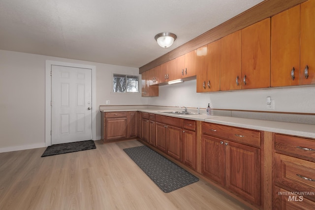 kitchen with a sink, brown cabinets, light wood finished floors, and light countertops